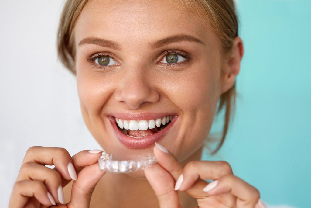 Blonde woman in Los Angeles about to put her clear aligner in her mouth to straighten her teeth. 