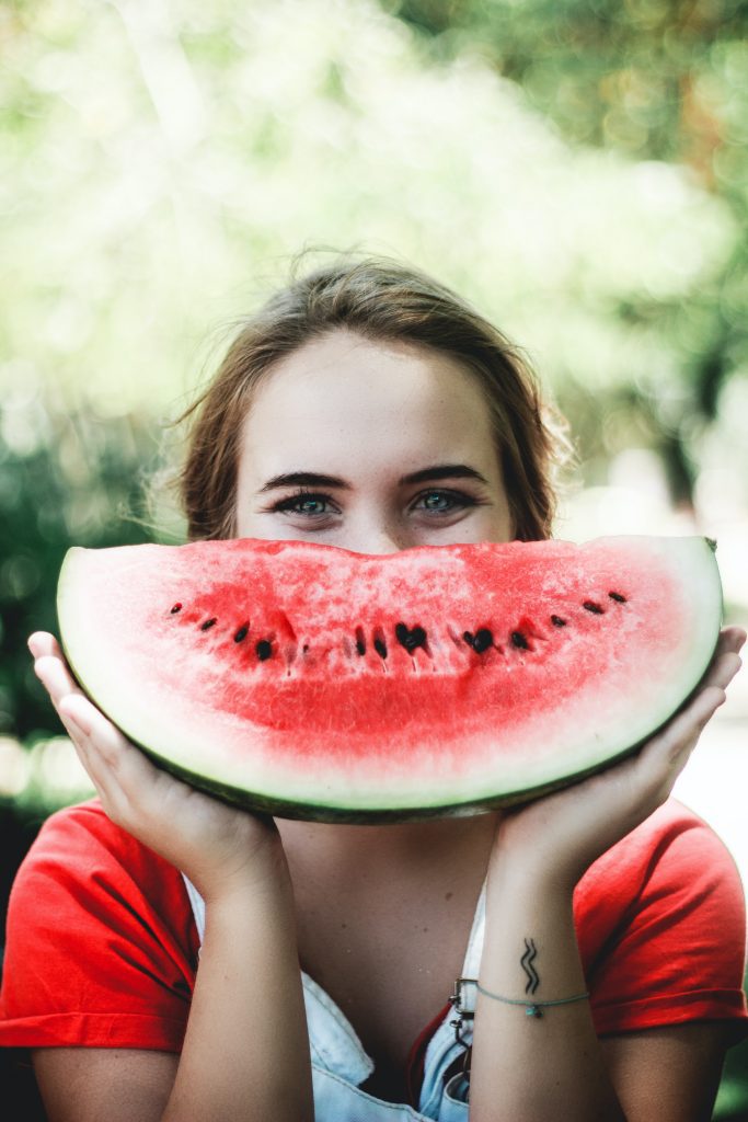 Orthodontic patient holding a slice of watermelon in front of her face as if it's a smile because she knows there are certain foods to avoid when wearing braces