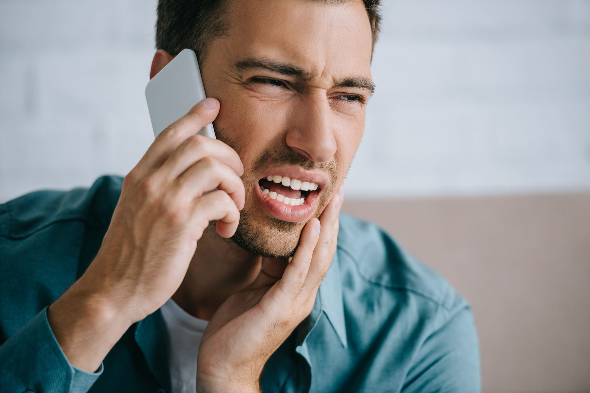 Man on phone with the Los Angeles orthodontist while holding his jaw appearing to be in pain.
