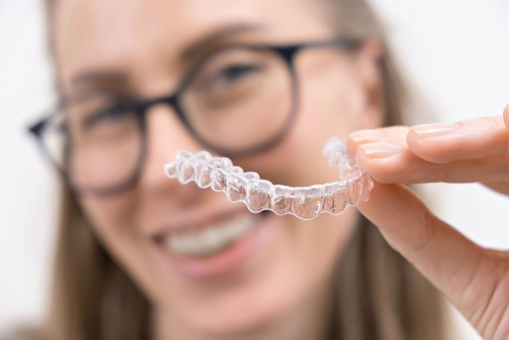 smiling woman holding up clear plastic removable aligner