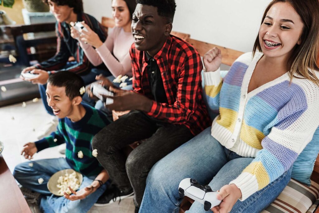 A bunch of teens playing video games, smiling and eating popcorn while straightening their teeth with clear aligners and clear braces