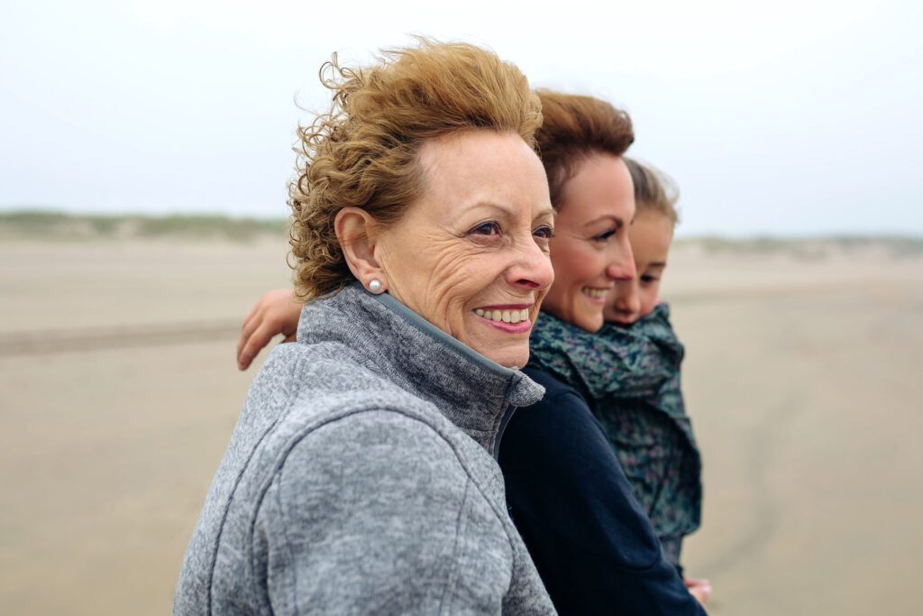 three generations of smiling women Los Angeles Senior woman with her daughter and granddaughter smiling while walking down a beach after Orthodontic Treatment Los Angeles