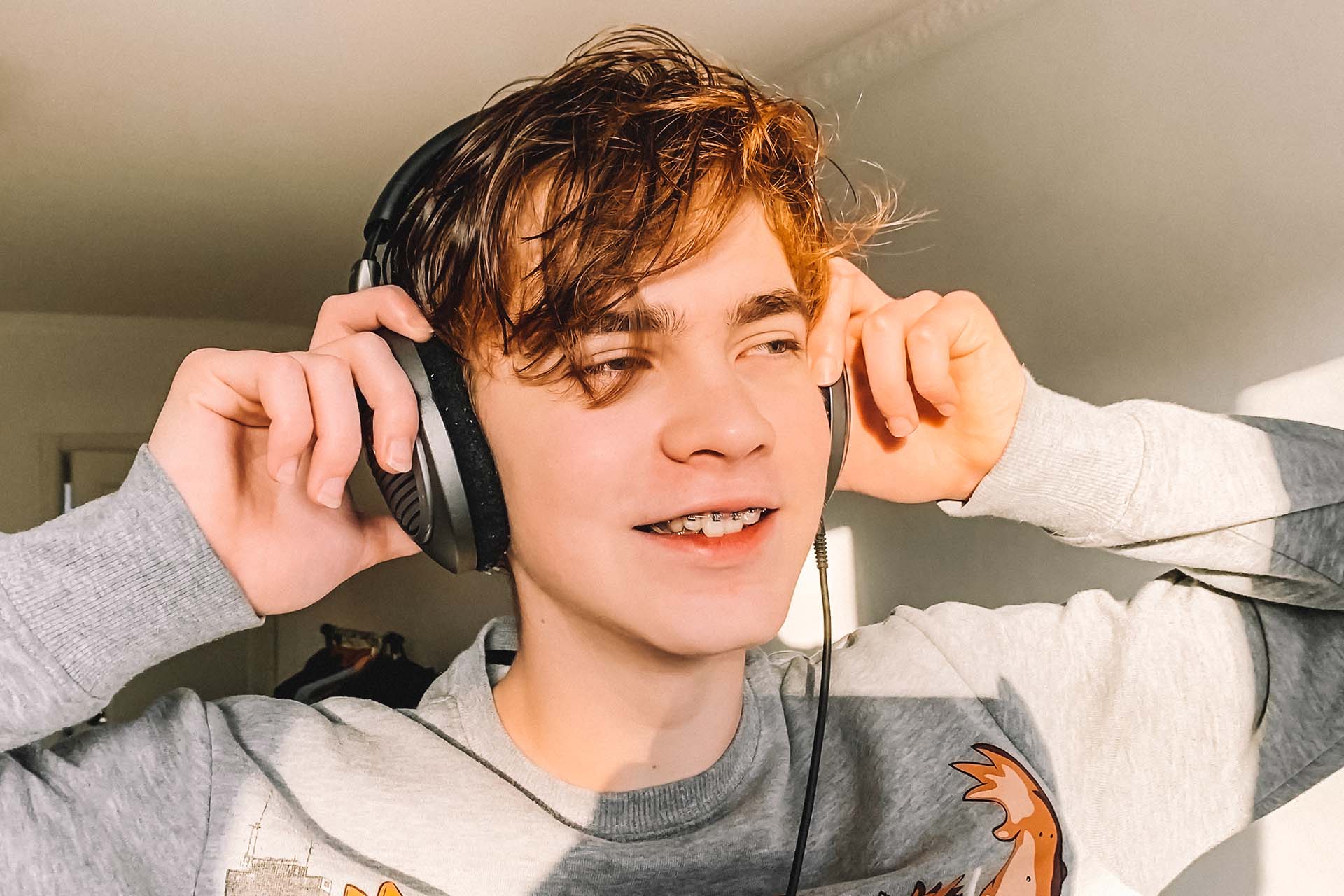 Teen boy with braces listens to music on headphones in Bel Air, Los Angeles, CA