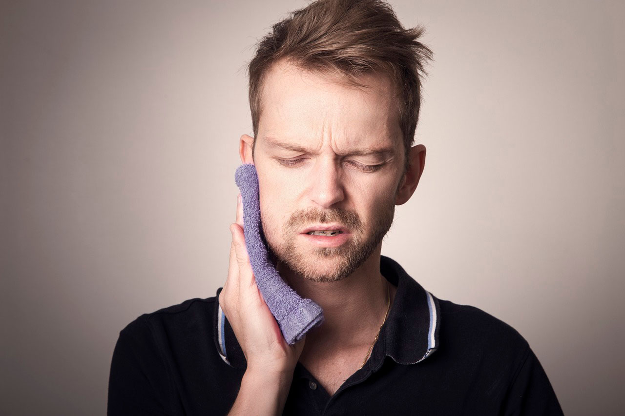 Brentwood, Los Angeles man holding purple towel to jaw as a cold compress because jaw pain is a common symptom of a TMJ disorder. 