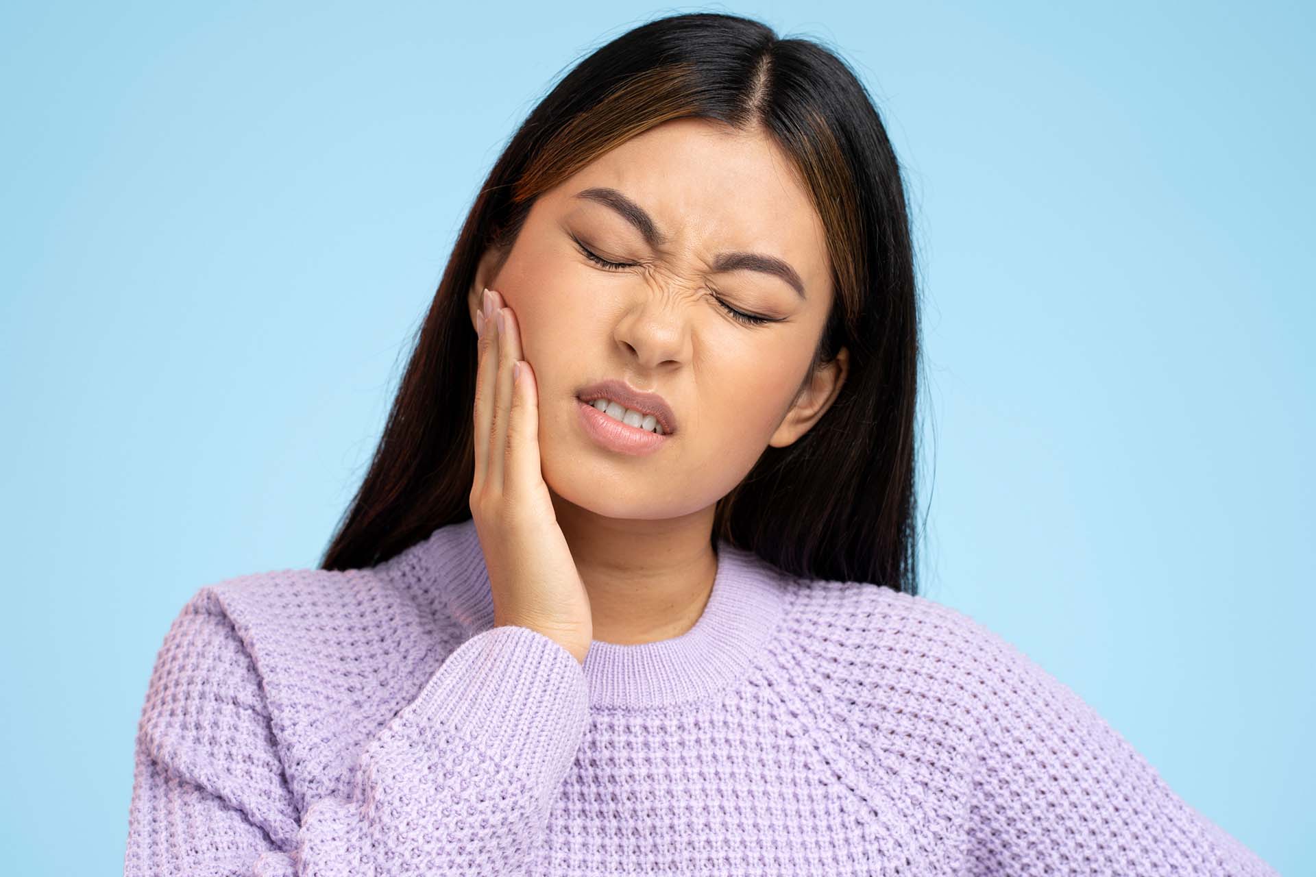 Culver City woman wincing and holding her lower jaw as she looks for a TMJ specialist near Los Angeles to relief her facial pain.