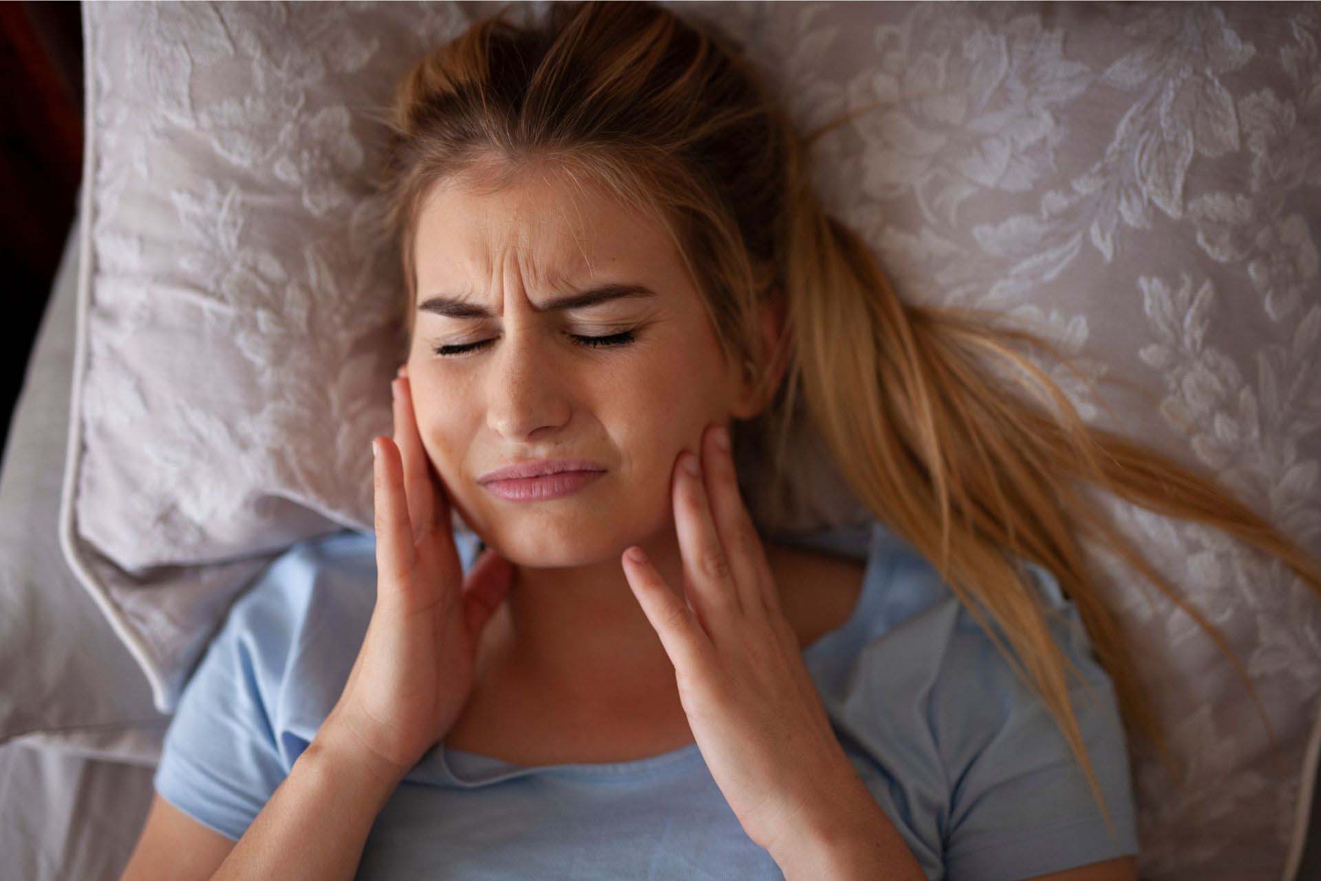 A Los Angeles, CA woman wincing in pain while holding her lower jaw due to facial pain and muscle pain when her mouth is in an open or closed position.
