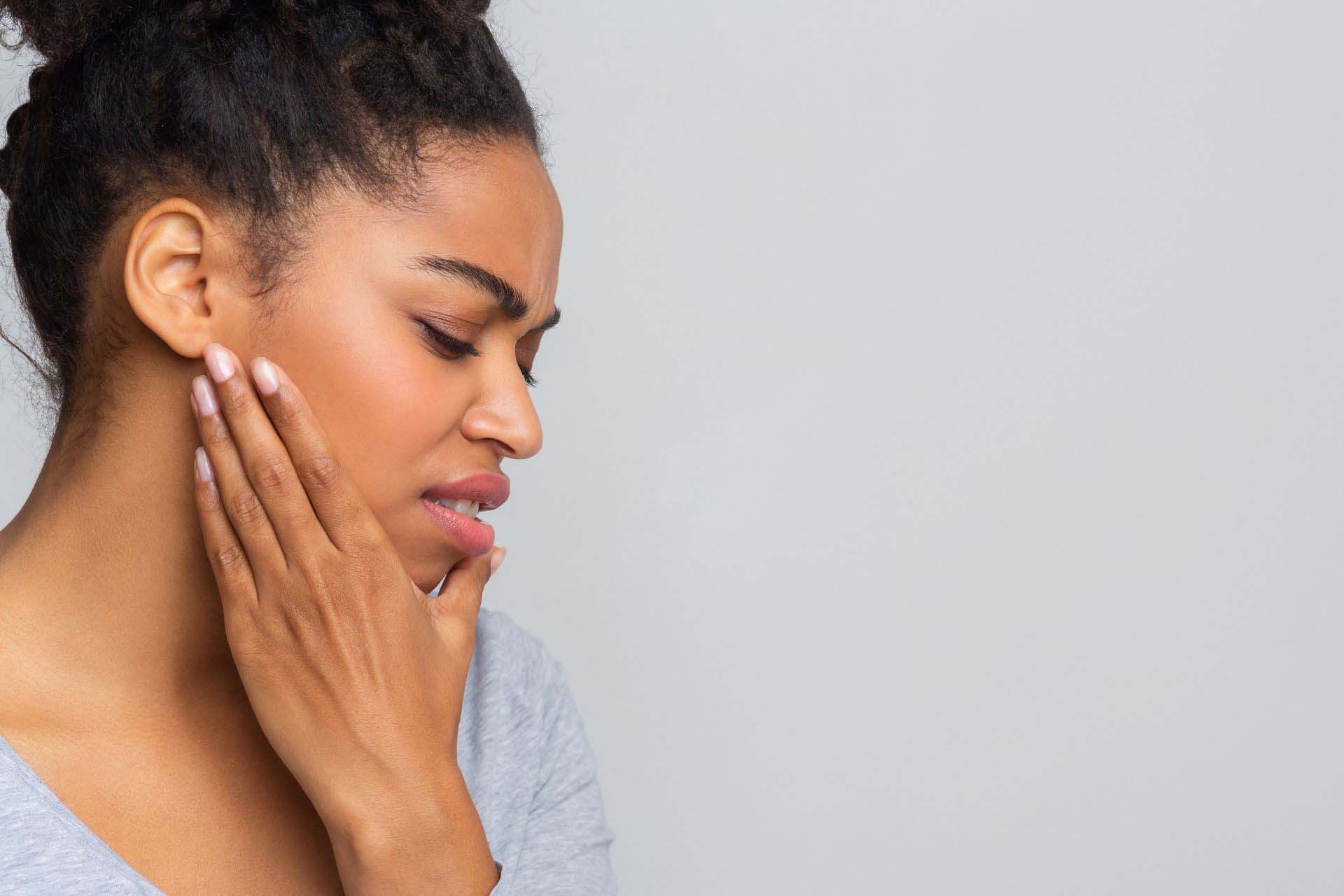 Woman holding jaw due to joint pain by her ears as she sees a TMJ specialist, Dr. Hakim near Brentwood, Los Angeles, who is treating TMJ for her.
