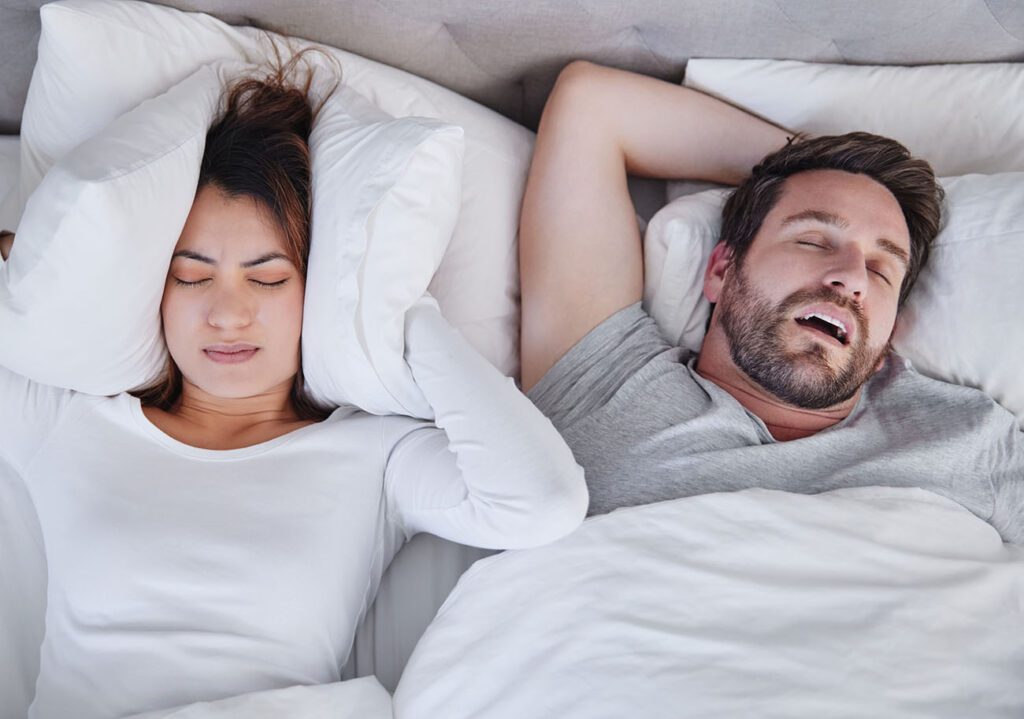 Snoring and sleep apnea can be a symptom of TMJ disorder as seen her with a man snoring and the woman covering her ears