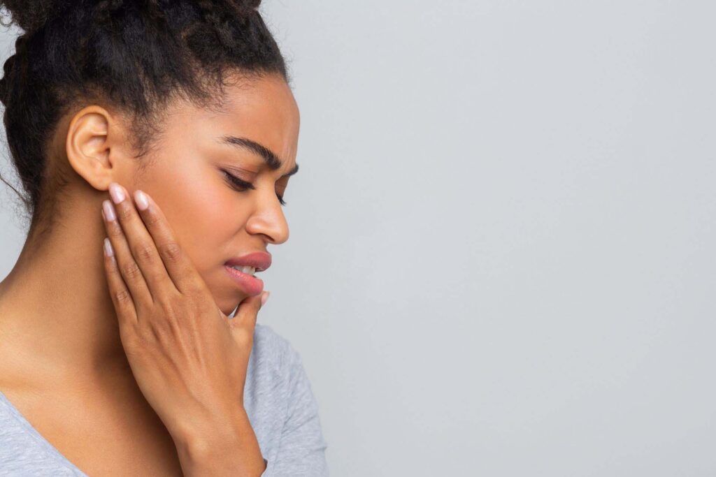 Woman holding jaw due to joint pain by her ears needing a TMJ specialist