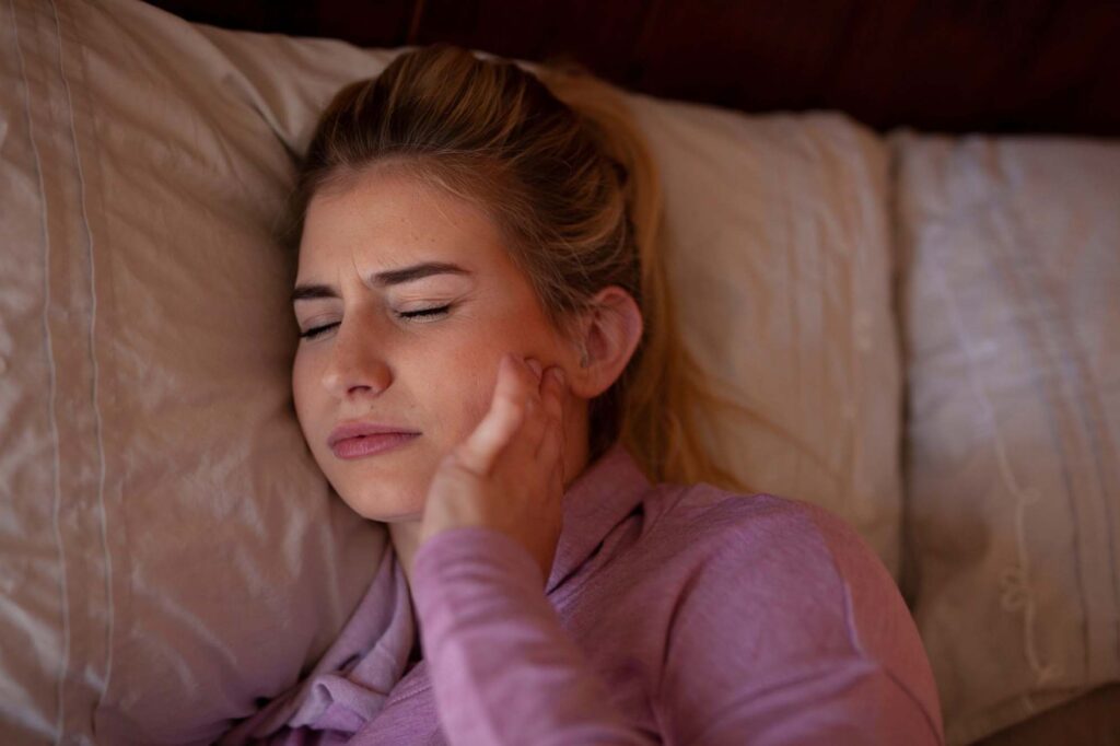 Young woman in bed experiencing chronic facial pain from a TMJ disorder