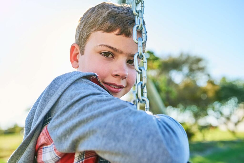 Little boy in need of early orthodontic treatment swings at the park